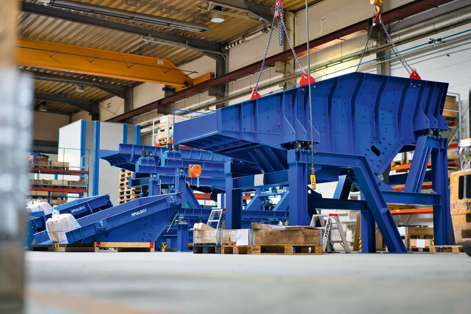 Blaue Aufgabeeinheiten und Förderrinnen für das Metallrecycling, hier die Materialzuführtechnik für das Material Schredderleichtfraktion. Das Bild zeigt die Produktion beim Hersteller SPALECK.