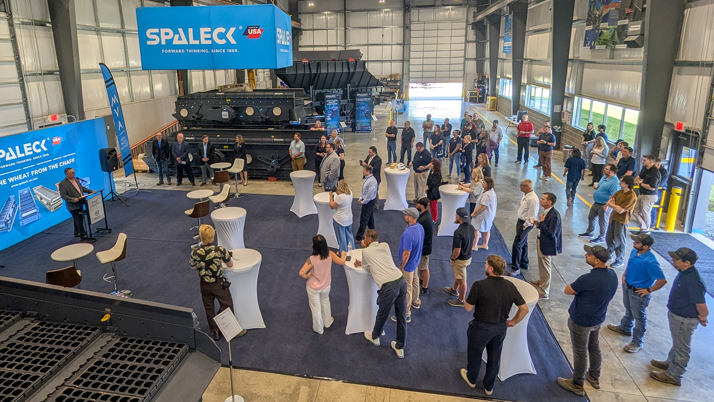 Besucher des Spaleck USA Opening Day hören bei offizieller Rede zu in der geschmückten Produktionshalle