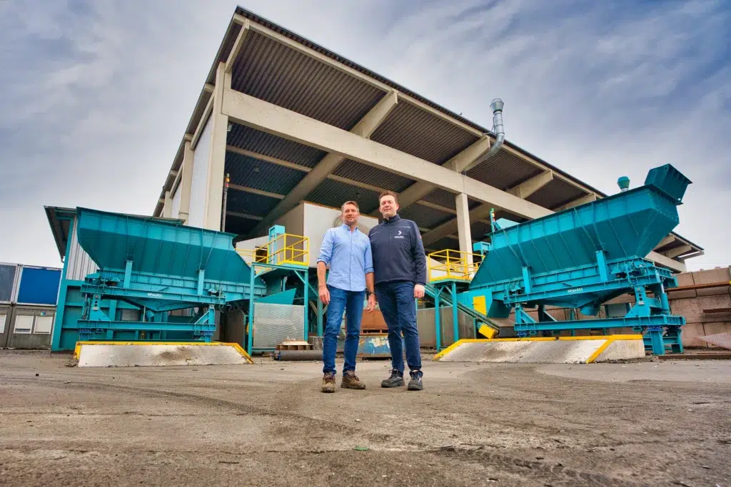 Michael Kannengießer (Koslow) und Christian Lake (SPALECK) stehen vor der Sensorsortieranlage für Metallrecycling. Links und rechts von ihnen steht jeweils ein SPALECK ActiveFEED Aufgabebunker, welche die Materialzufuhr für die Sortiergeräte im Metallrecycling optimieren.